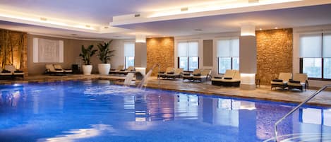 An indoor swimming pool with lounge chairs and a stone wall.