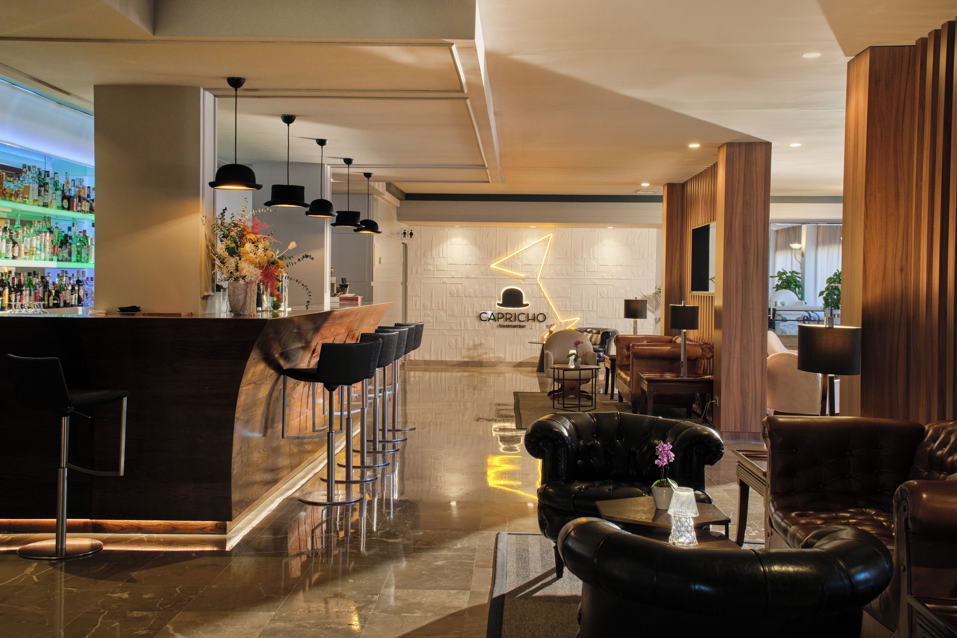 Un moderno bar con barra, varios taburetes y una zona de estar con sofás de cuero y una mesa de centro.