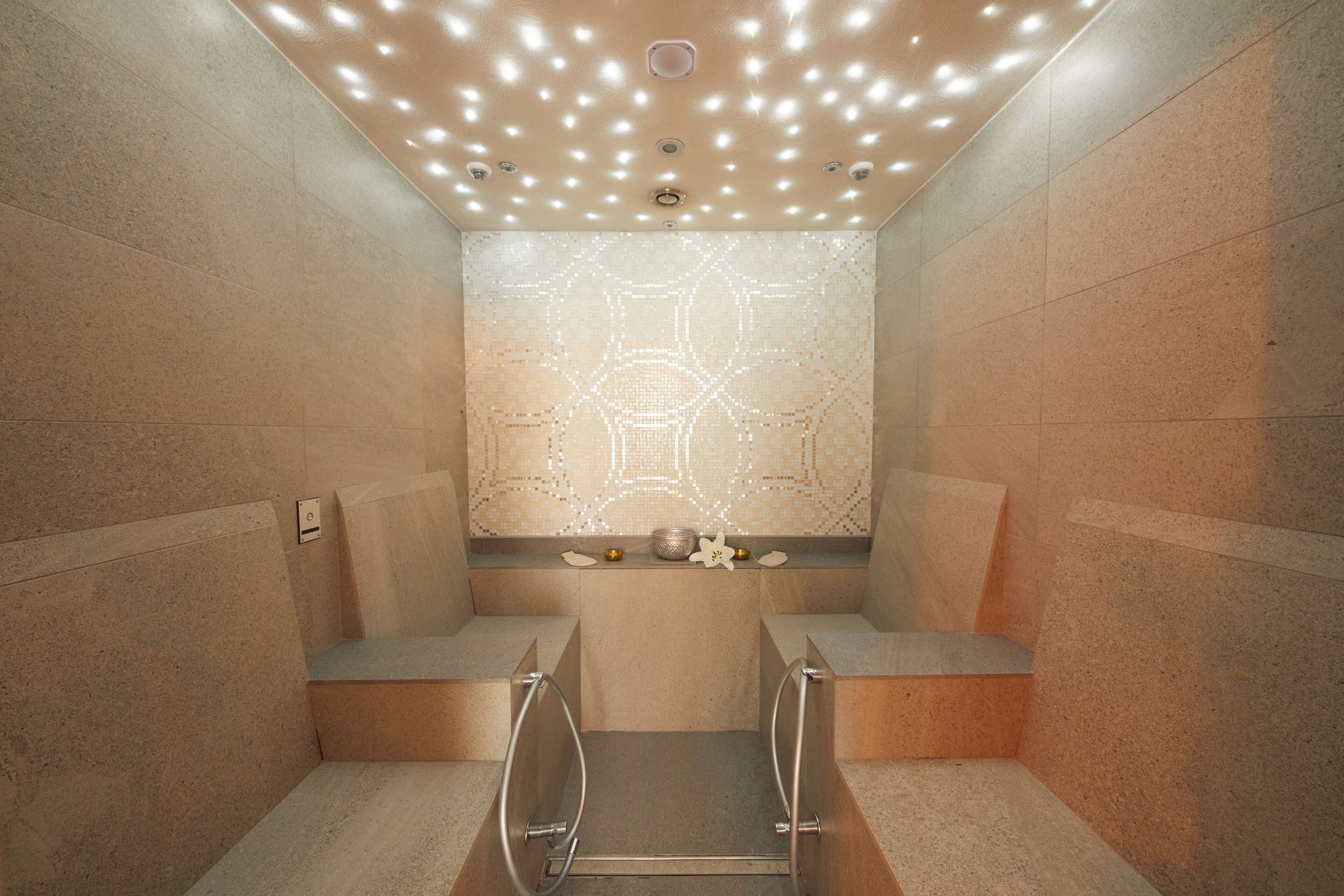 Un baño moderno con un revestimiento de pared de diseño geométrico, un pequeño estante con adornos y un banco empotrado.