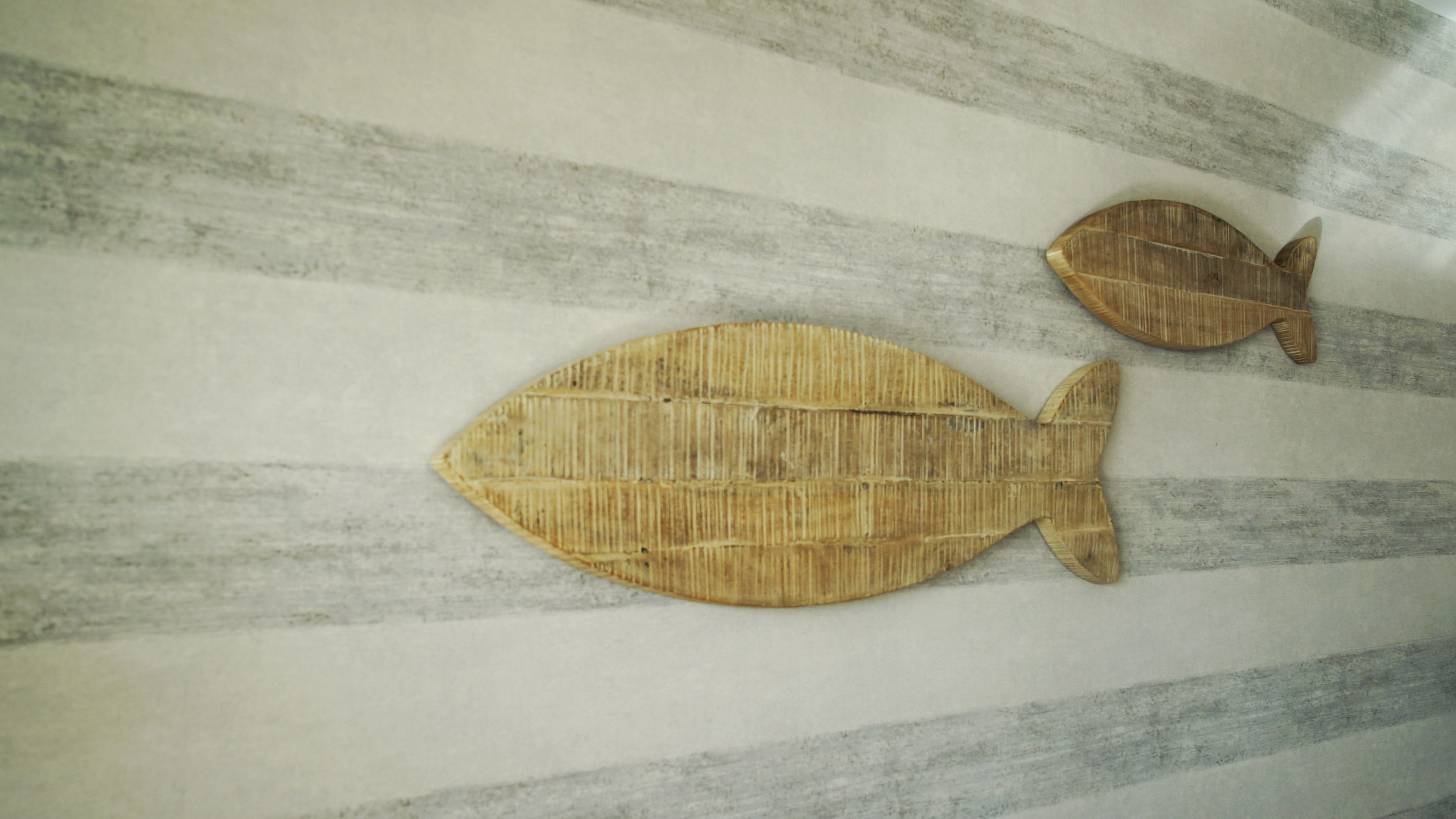 Two wooden fish wall decorations on a striped wall.