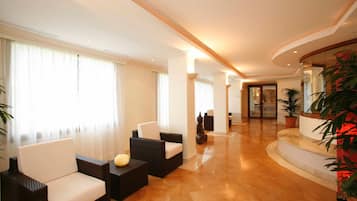 A spacious lobby with a high ceiling, a polished marble floor, and a seating area with wicker sofas and a small table.