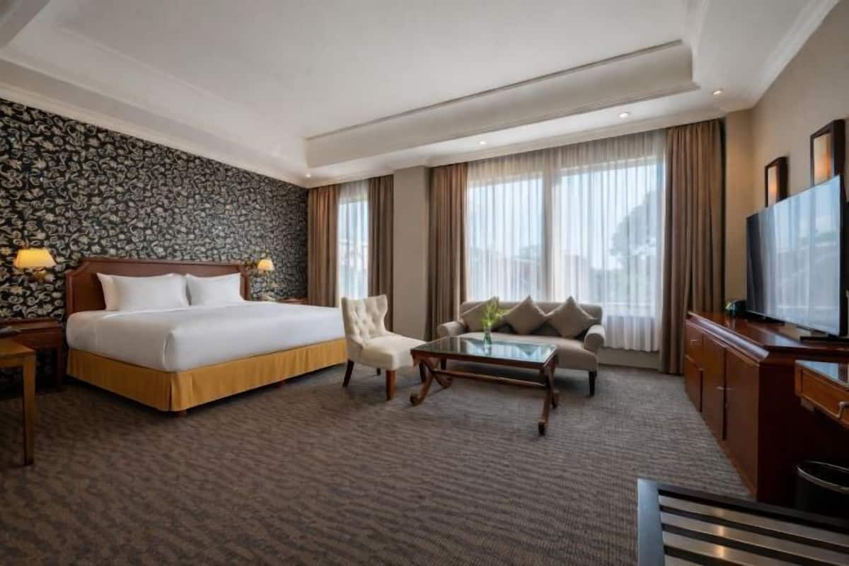 A hotel room with a bed, a sofa, a coffee table, a TV, and a patterned wall.