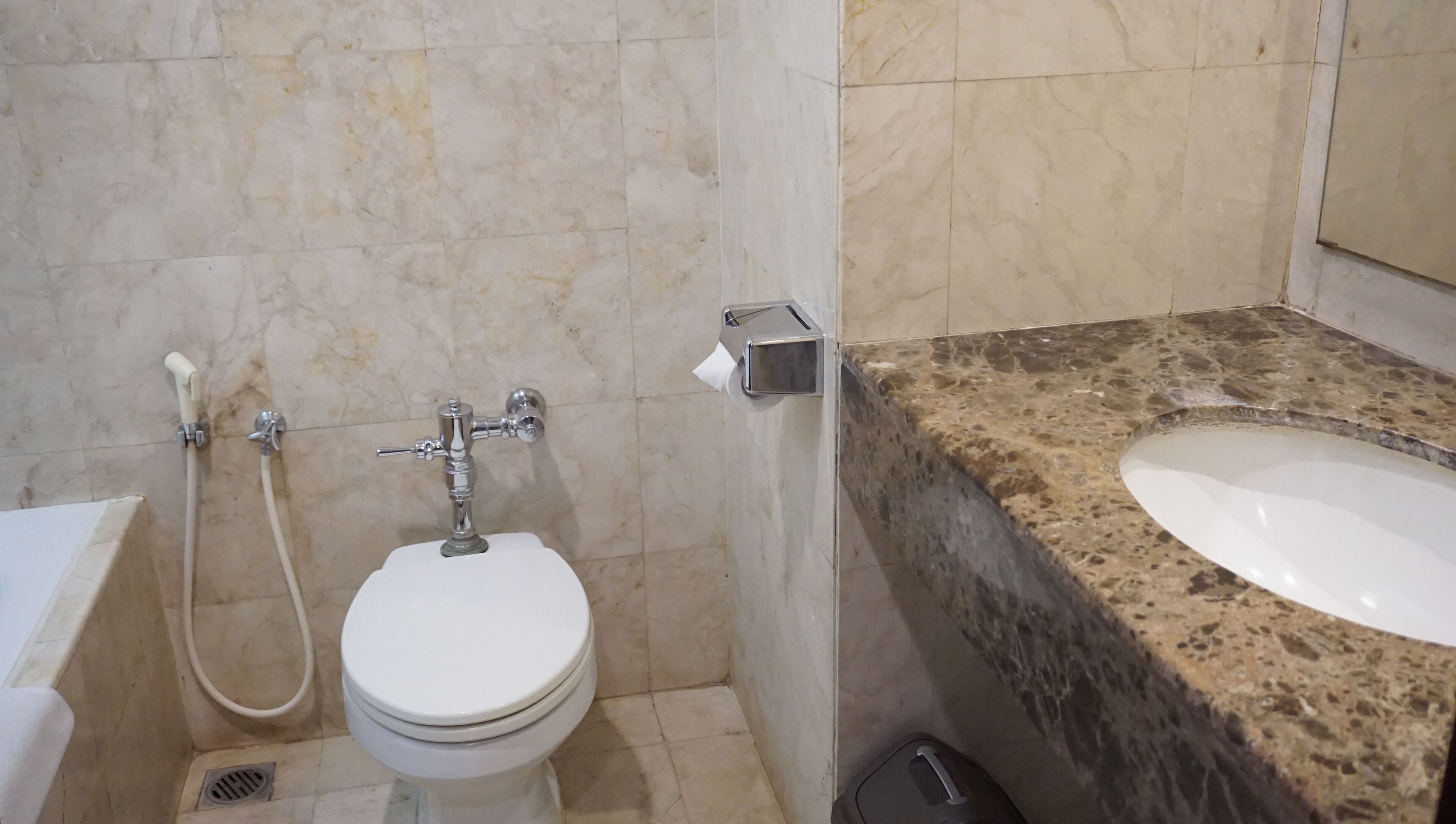 A bathroom with a toilet, a bidet, a paper towel dispenser, and a sink with a granite countertop.