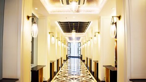 A hotel corridor with a patterned floor, wall-mounted light fixtures, and a ceiling light.