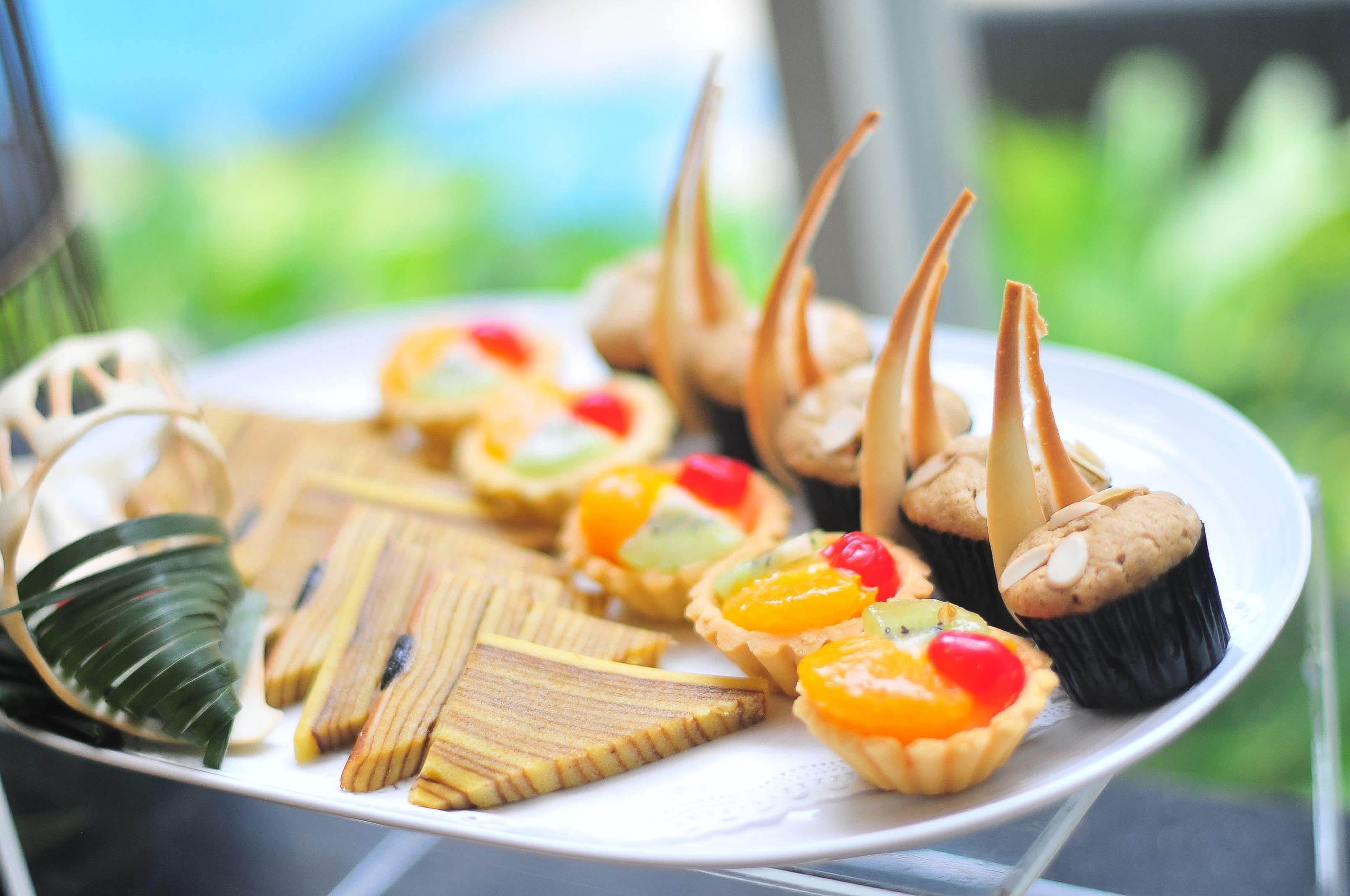 A plate of assorted pastries and cookies, including fruit tarts and almond-topped cupcakes, on a white plate.