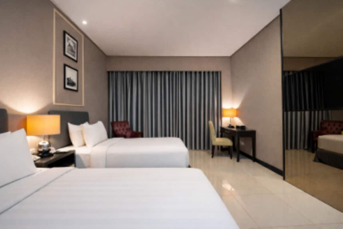 A hotel room with two beds, a desk, a chair, a lamp, and a large mirror.