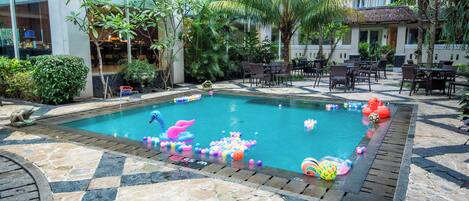 A swimming pool with colorful balls and inflatable toys, surrounded by palm trees and outdoor seating.