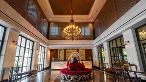 A spacious lobby with a grand chandelier, a reception desk, and a plush red seating area.
