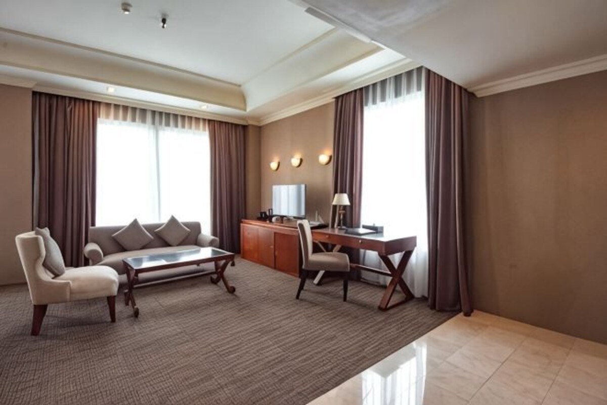 A hotel room with a sofa, armchair, desk, and lamp.
