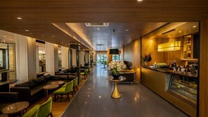 A modern hotel lobby with a long reception desk, comfortable seating areas, and a central decorative plant.