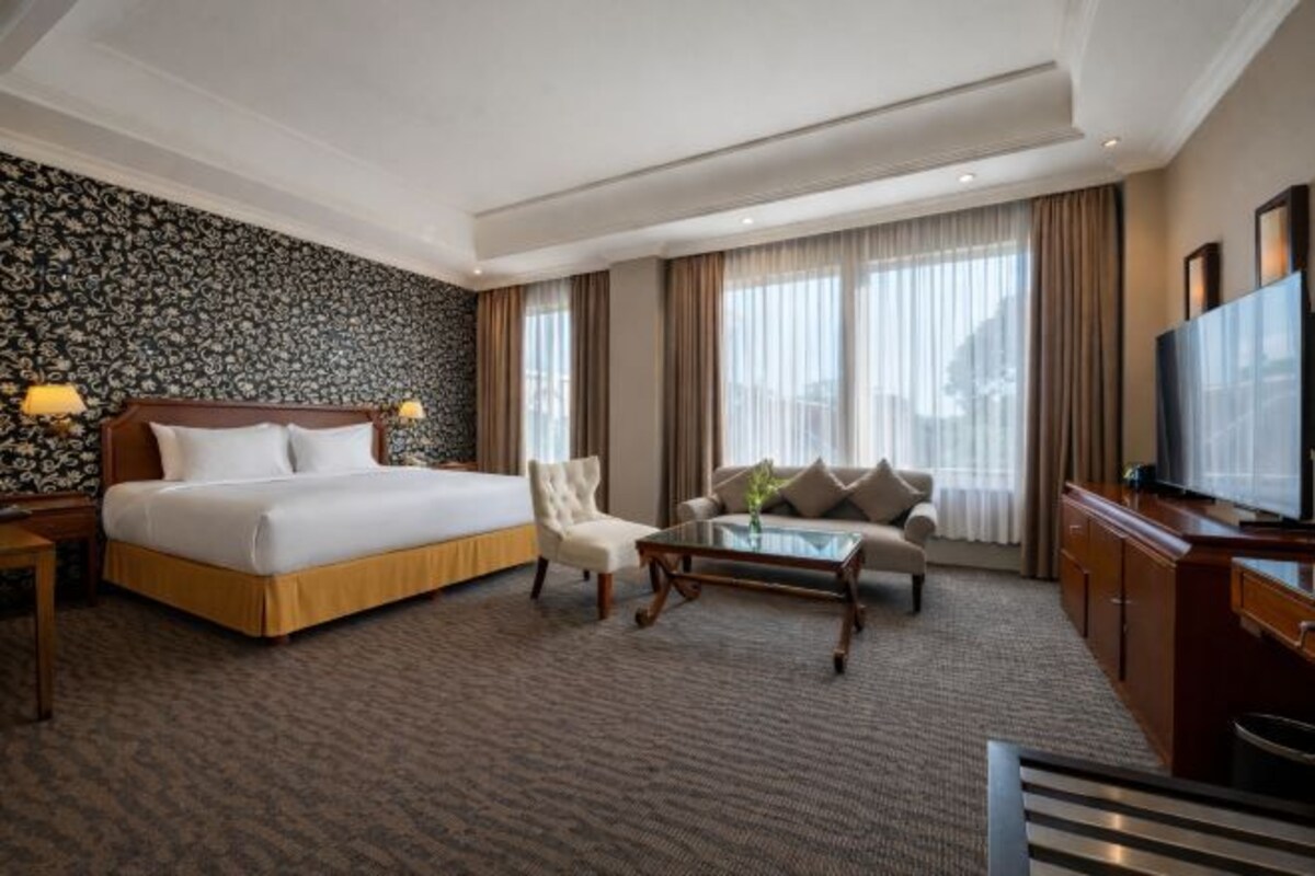 A hotel room with a bed, a sofa, a coffee table, a TV, and a patterned wall.