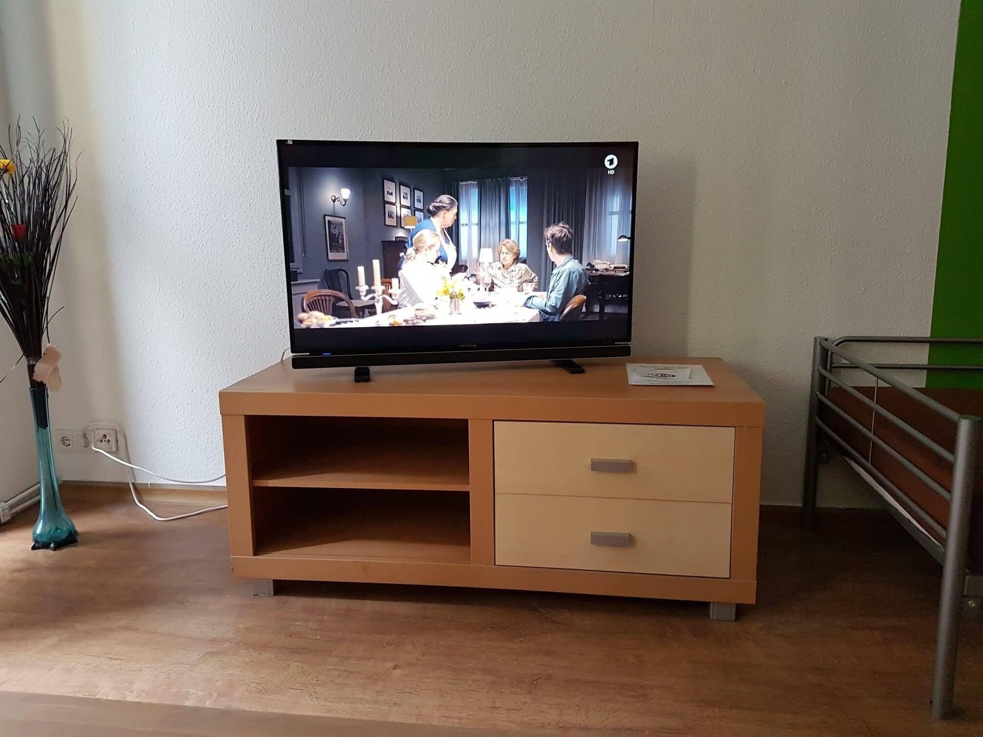Ein Fernseher auf einer Holzkabinet mit einer Schublade, eine Vase mit Blumen und eine grüne Wand.