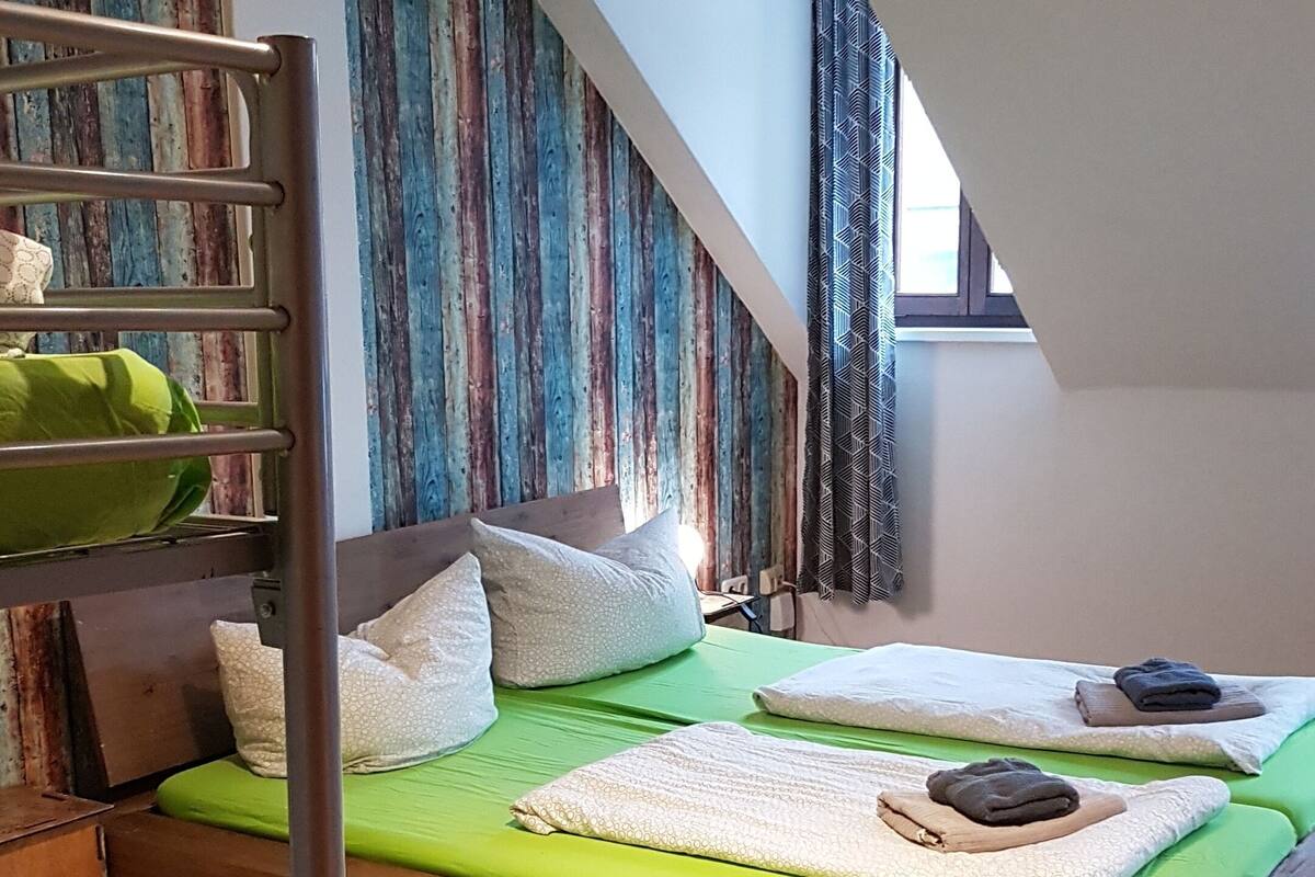 A loft-style bedroom with a sloped ceiling, a bunk bed, and a green mattress.