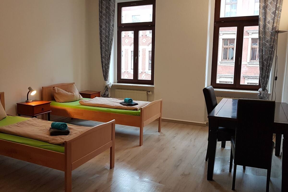 A room with two wooden beds, a desk, and a chair.