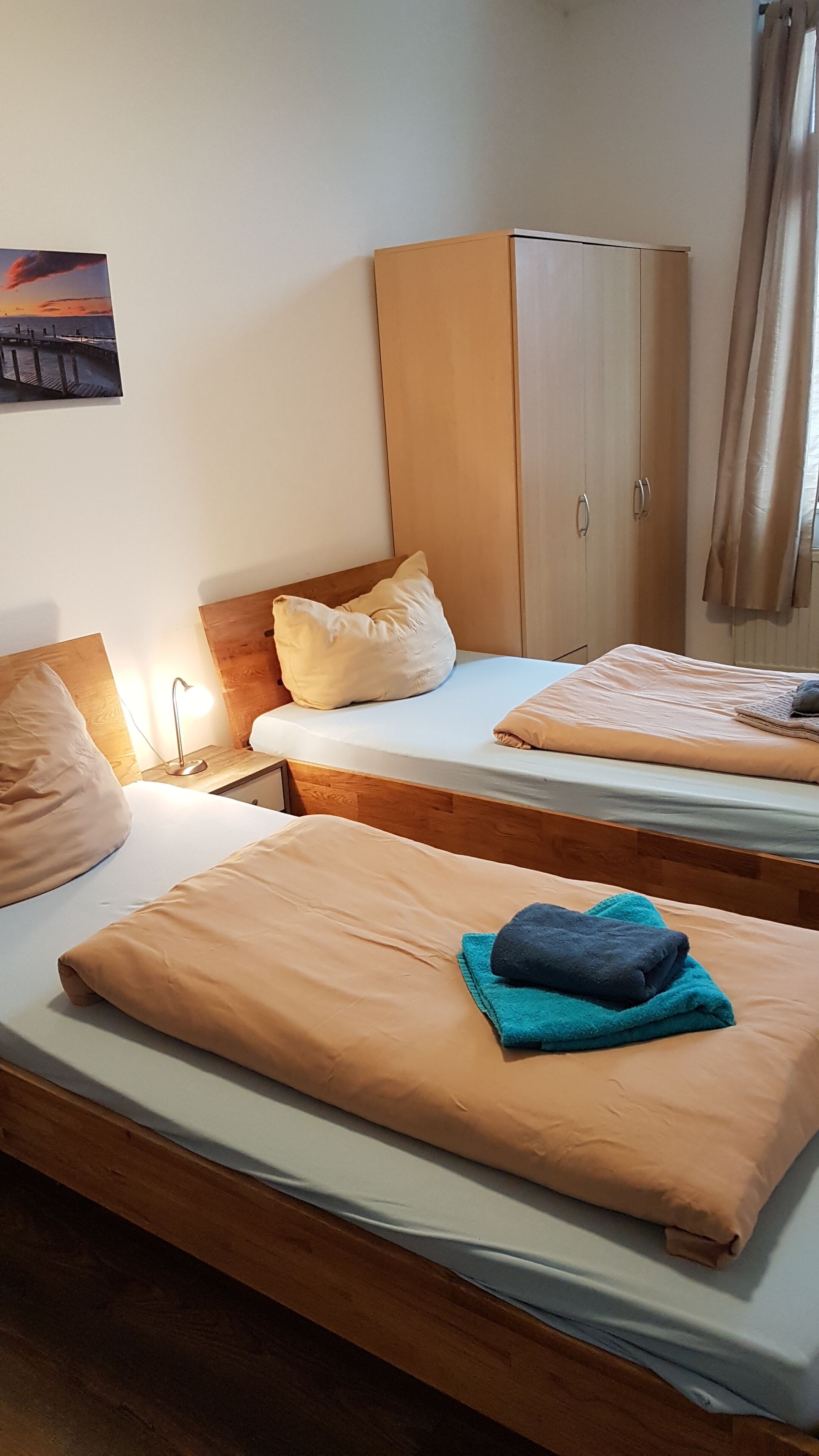 A hotel room with two beds, wooden headboards, a wardrobe, and a painting on the wall.