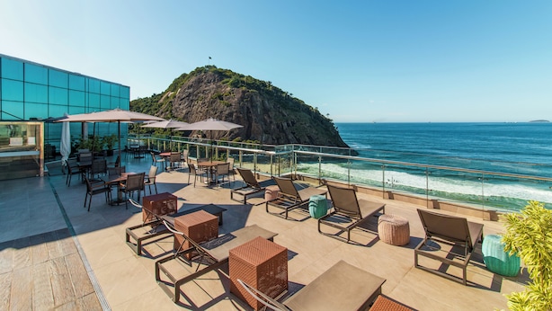 Eine Dachterrasse mit Außenmöbeln, Blick auf das Meer und eine felsige Insel im Hintergrund.