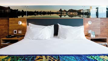 A hotel room with a large bed, two bedside tables, a nightstand, a cityscape view, and a wooden headboard.