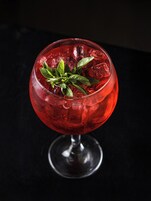 A cocktail glass with a red drink, ice cubes, and a garnish on a dark surface.