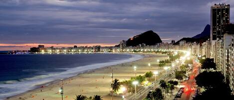 Un paysage urbain côtier avec une plage, une montagne imposante et un grand immeuble doté de nombreuses fenêtres.