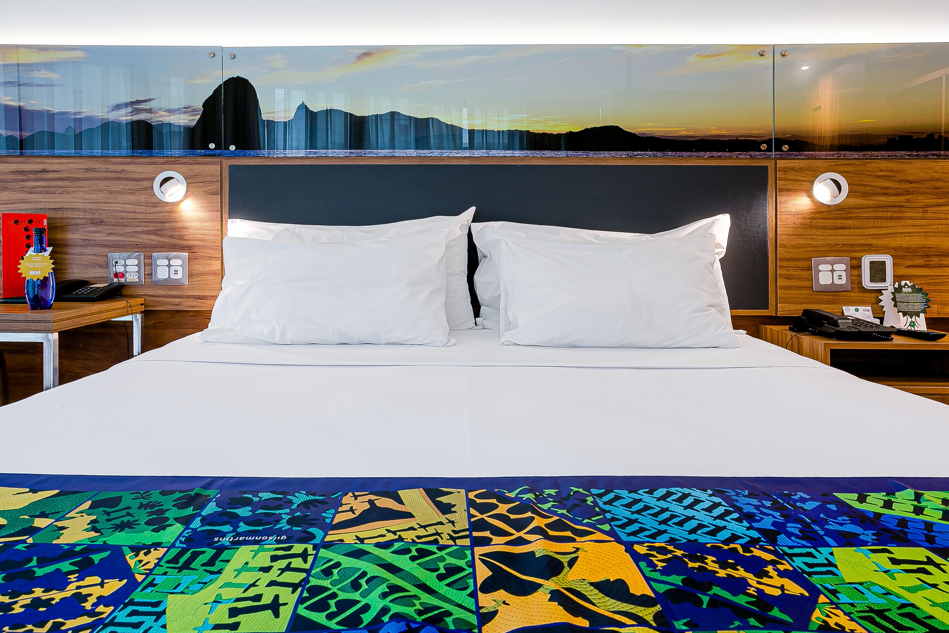 Ein Hotelzimmer mit einem großen Bett, zwei Nachttischen und Blick auf eine Stadtlandschaft bei Sonnenuntergang.