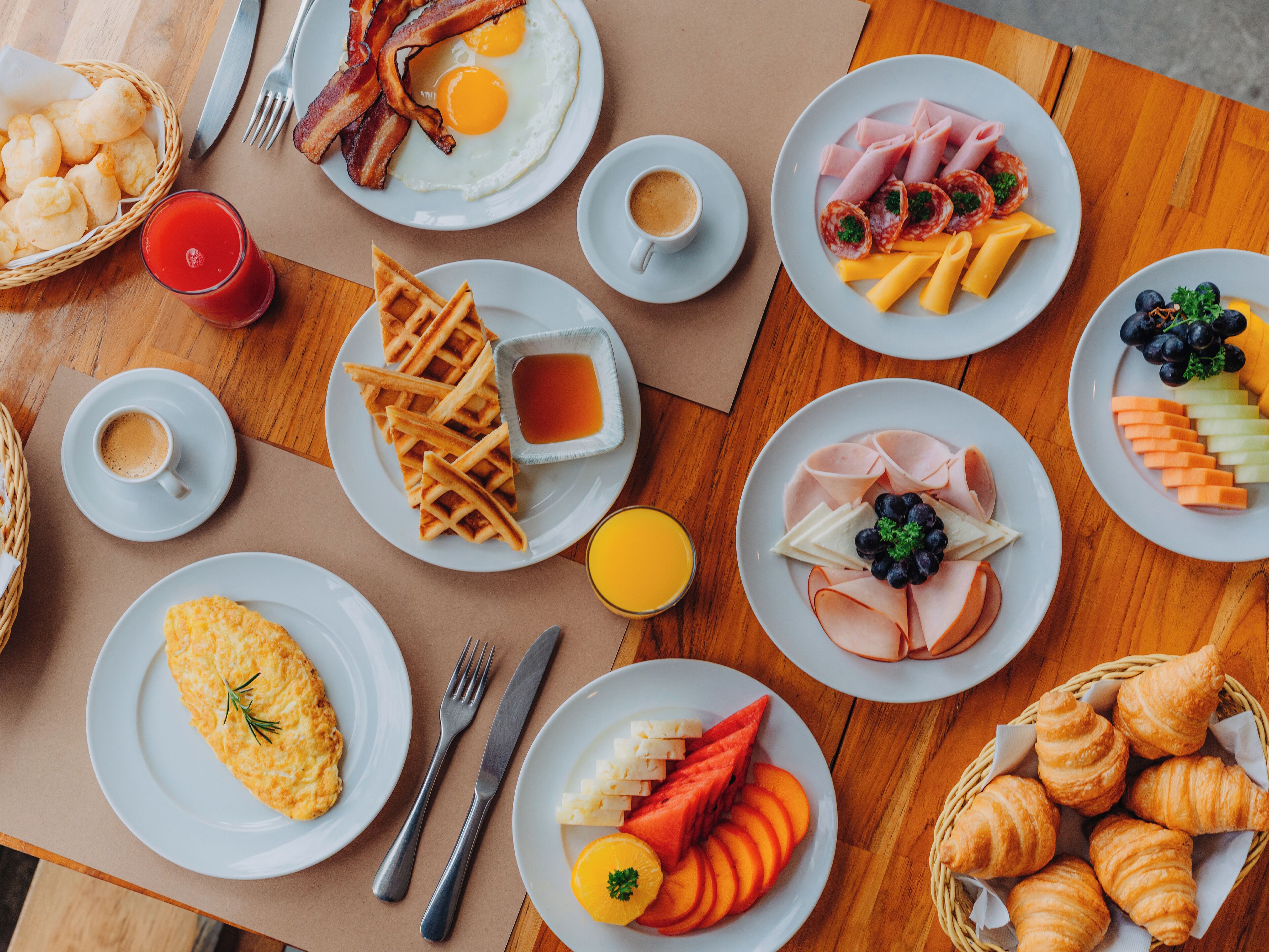 Un bufé de desayuno con diversos platos, incluyendo huevos, gofres, jamón, queso y bollería.