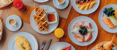 Un bufé de desayuno con diversos platos, incluyendo huevos, gofres, jamón, queso y bollería.