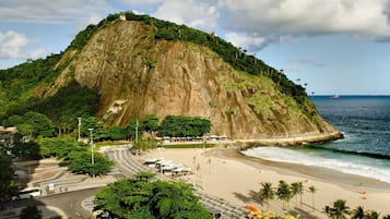 A coastal cityscape with a prominent hill, a beach, and a road leading to a parking area.