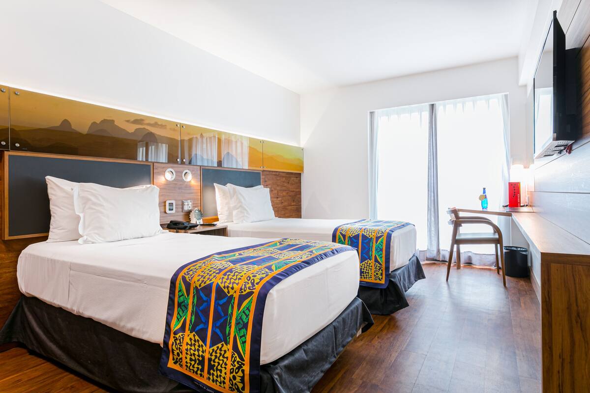 Quarto de hotel com duas camas, uma escrivaninha e uma televisão.
