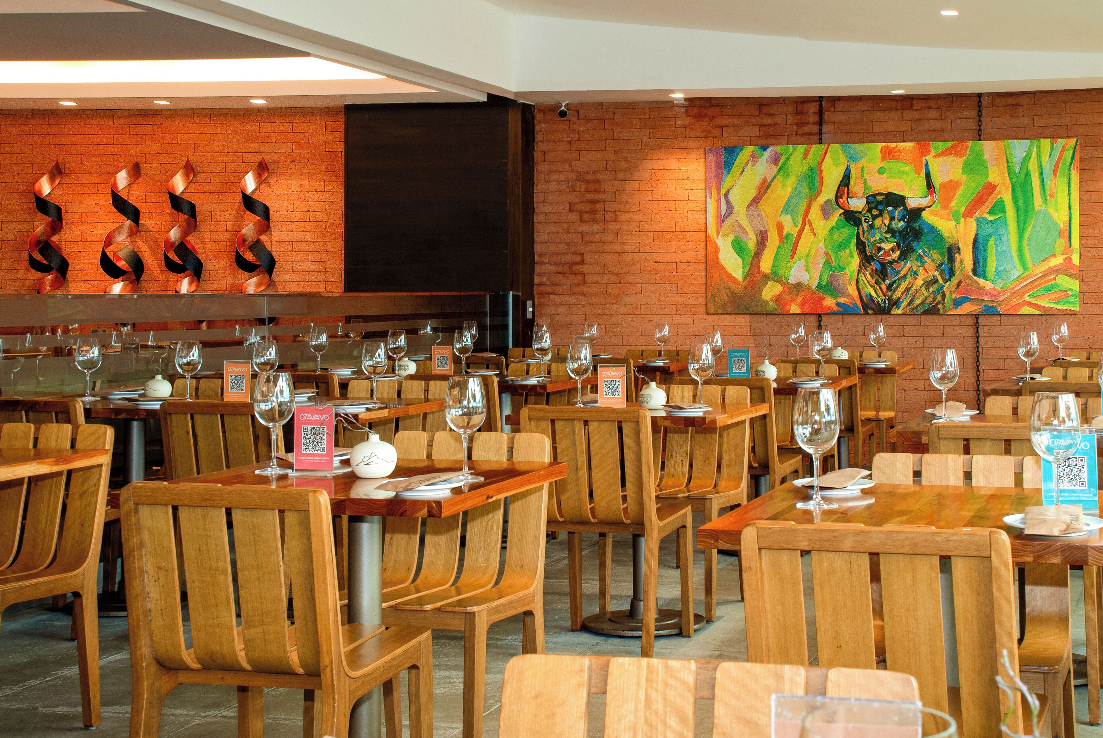 A restaurant with wooden tables and chairs, QR codes on menus, and a bull painting on the wall.