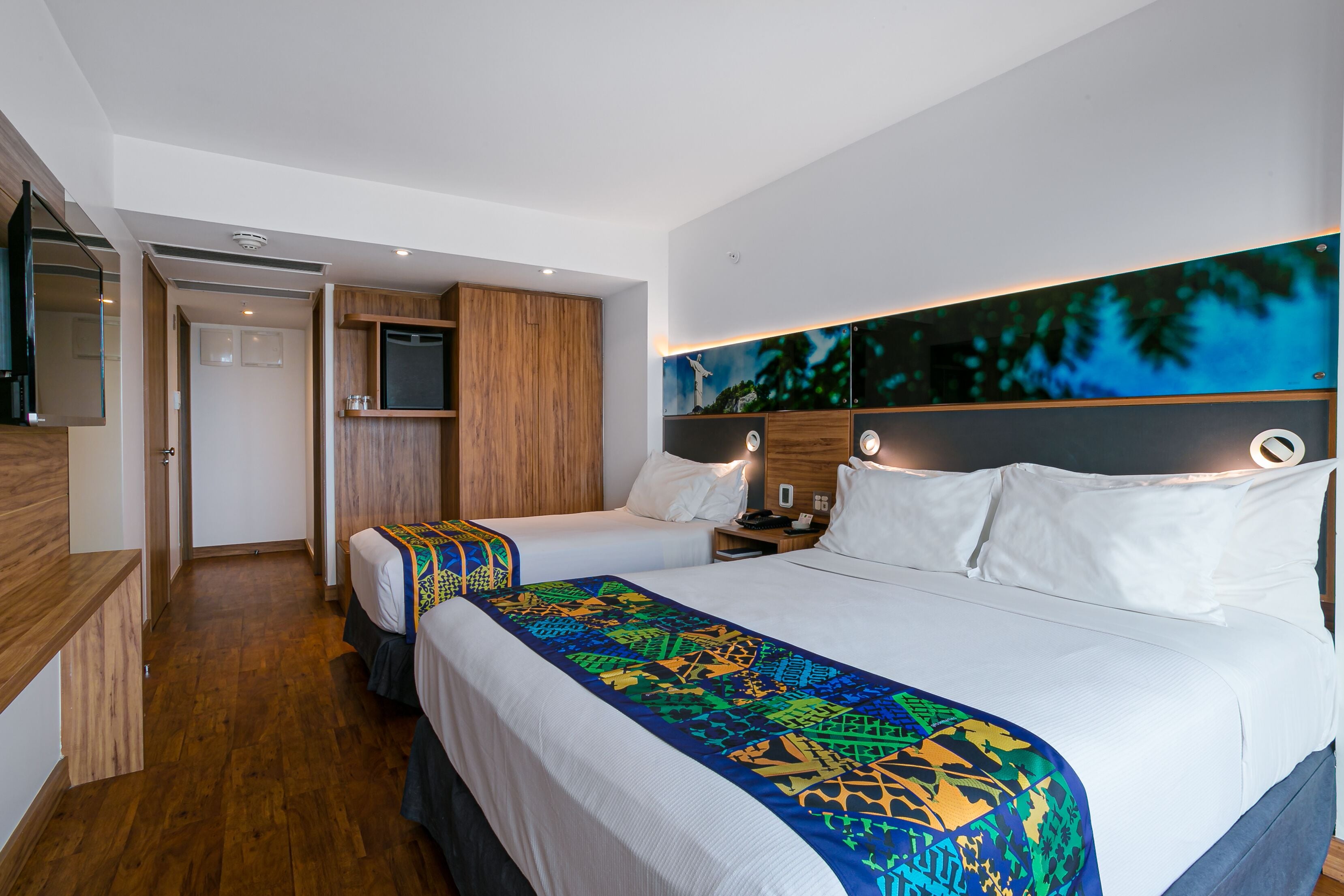 Habitación de hotel con dos camas, televisión, armario de madera y un cuadro grande en la pared.
