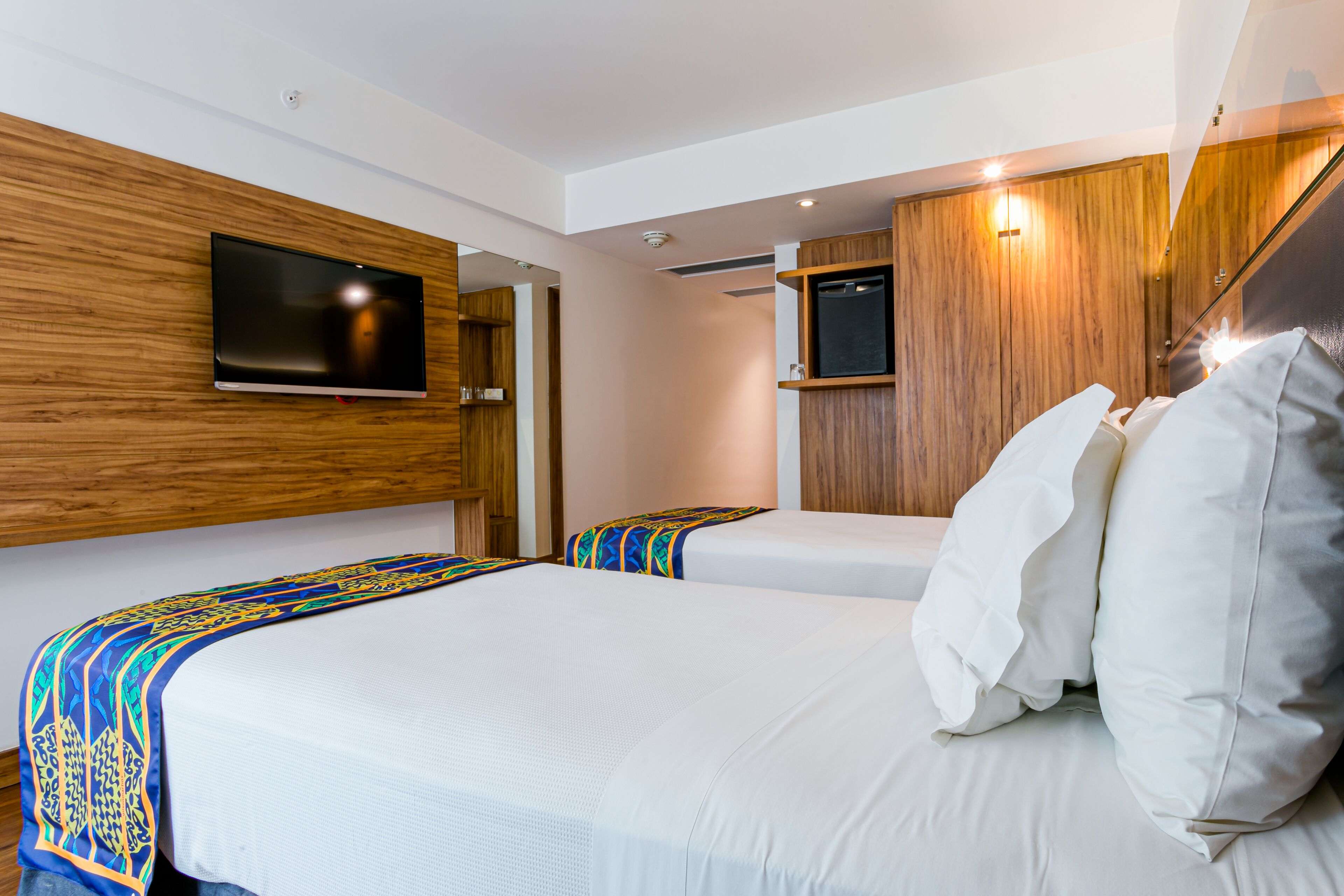 Quarto de hotel moderno com duas camas, uma televisão de tela plana na parede e um painel de parede em madeira.