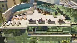 Ein modernes Gebäude mit Pool auf dem Dach, Außenbereich und einer Glasfassade, die die Umgebung widerspiegelt.