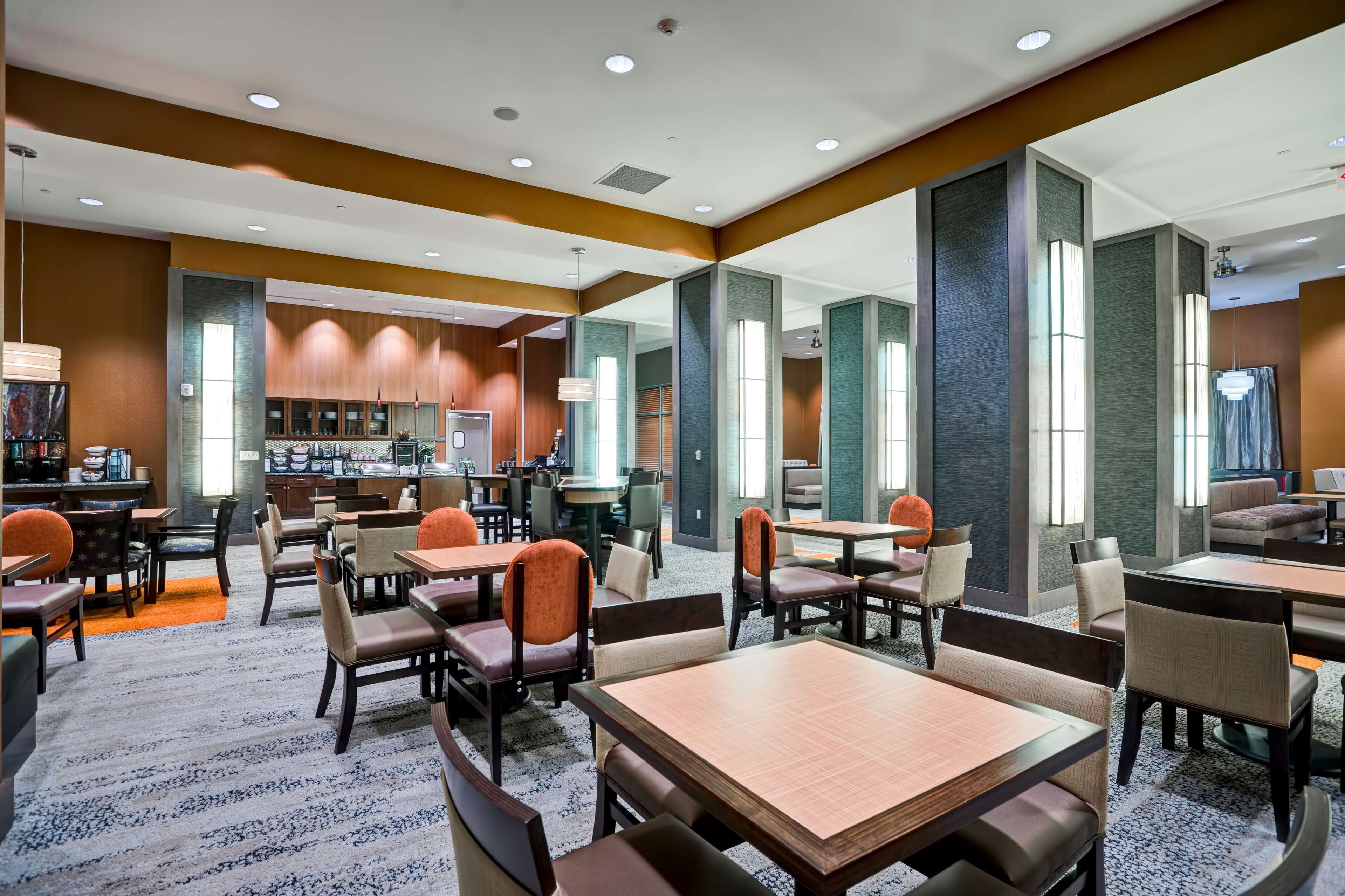 A hotel lobby with multiple seating areas, a reception desk, and a kitchen in the background.