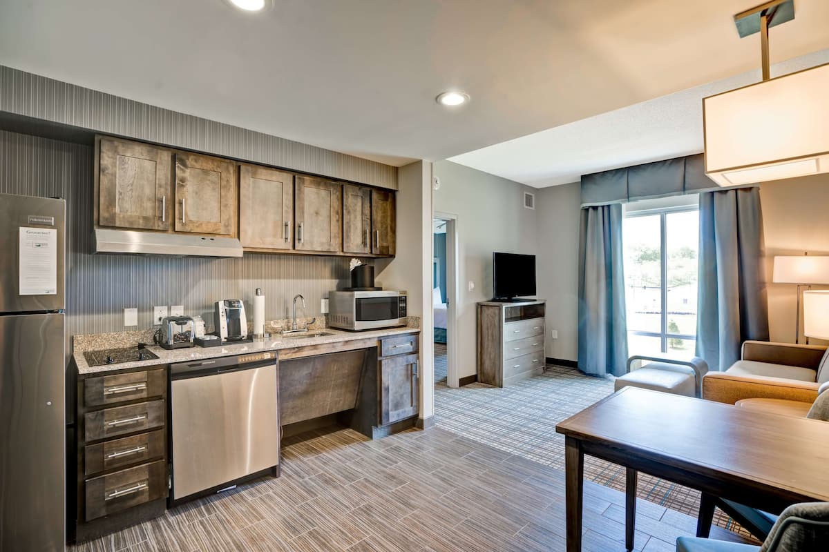 A modern kitchen with stainless steel appliances, a built-in microwave, and a dishwasher. There is a dining area with a table and chairs, and a TV mounted on the wall.
