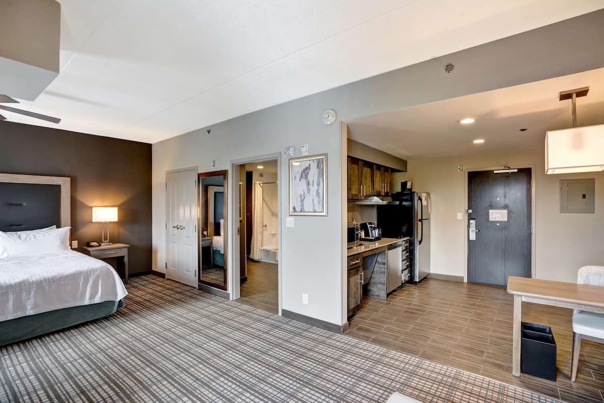 A hotel room with a bed, a desk, a kitchenette, and a bathroom.