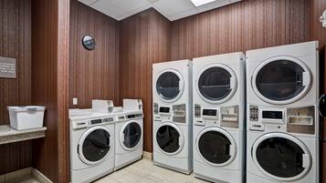 A laundry facility with four stacked washing machines, a clock, and a sign indicating product availability.