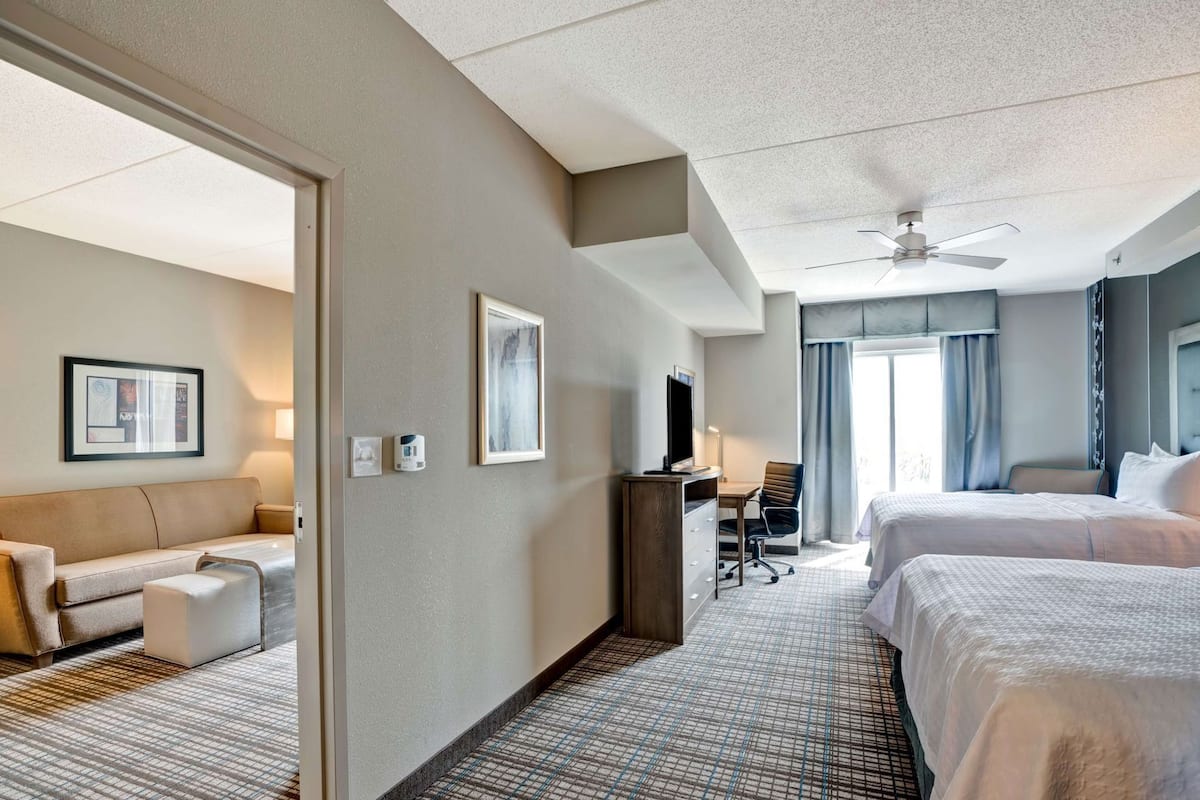 A hotel room with a bed, a desk, a chair, a television, and a ceiling fan.