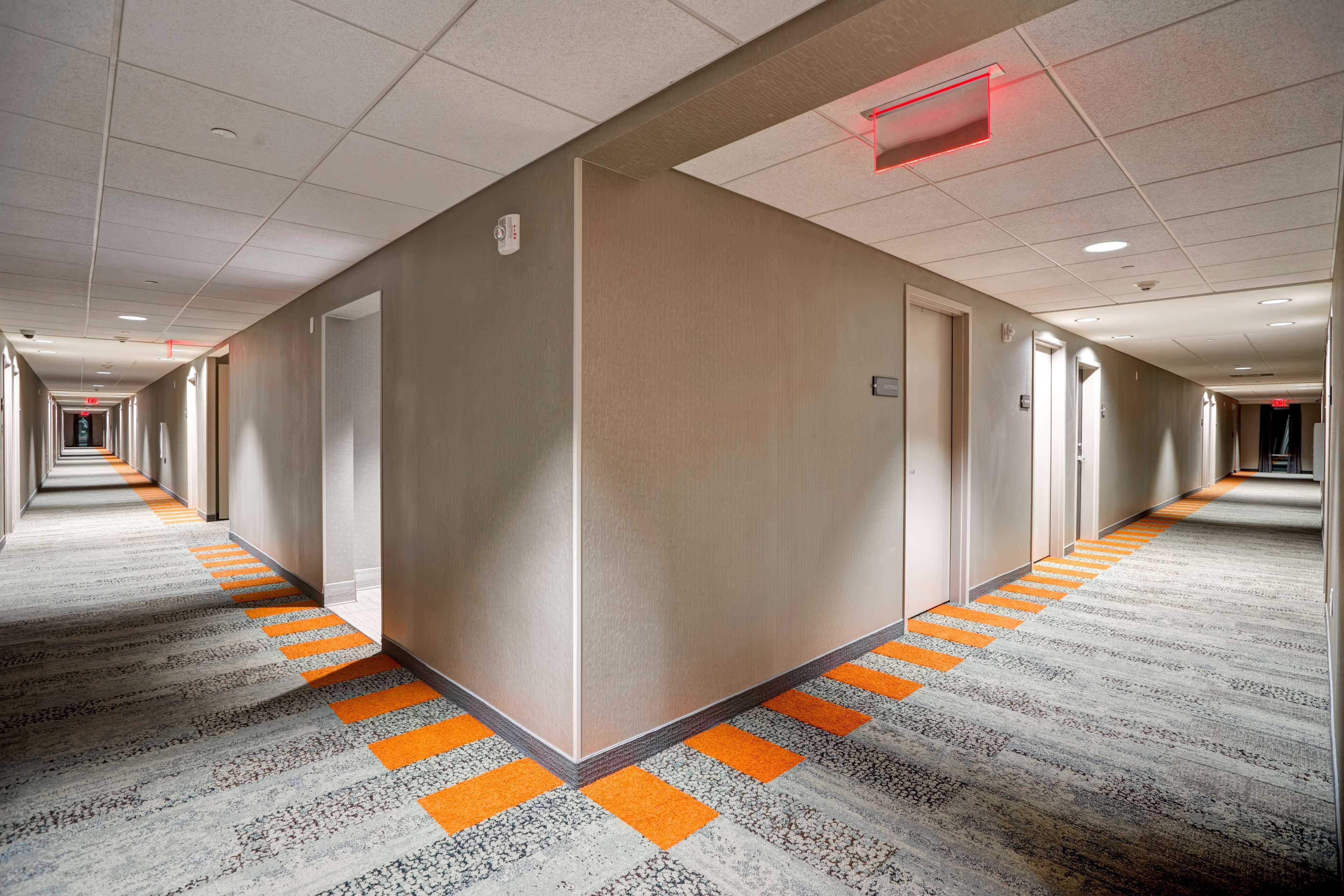 A long, narrow hotel corridor with a patterned carpet and orange safety lines.