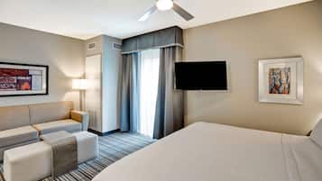 A hotel room with a bed, a sofa, a TV, a ceiling fan, and artwork on the walls.