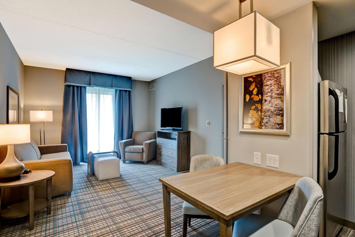 A hotel room with a dining area, a TV, a refrigerator, and a painting on the wall.