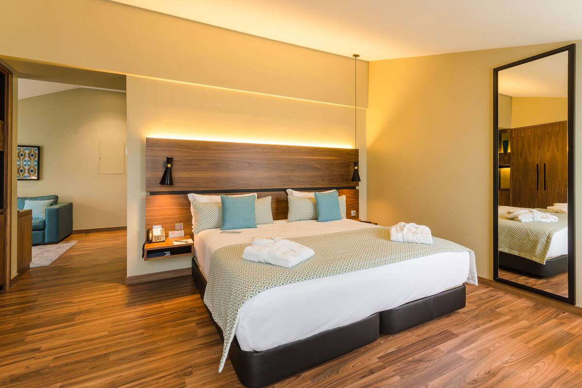 A hotel room with a large bed, bedside tables, a mirror, and a wooden floor.