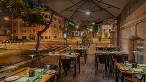 An outdoor dining area with tables set for two, under a canopy, overlooking a street with buildings and a pedestrian crossing. - Hotel Vincci Liberdade (Lisbon)
