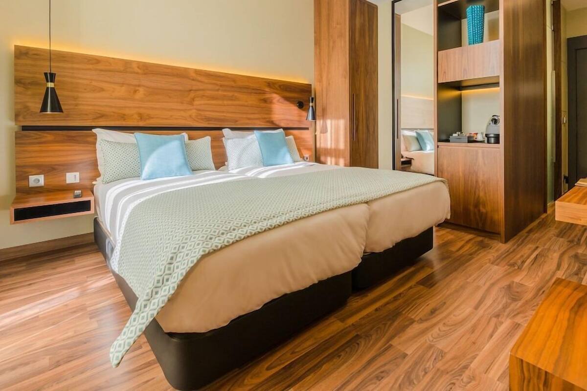 A modern bedroom with a wooden headboard, a bed with patterned bedding, a bedside table, and a wardrobe.