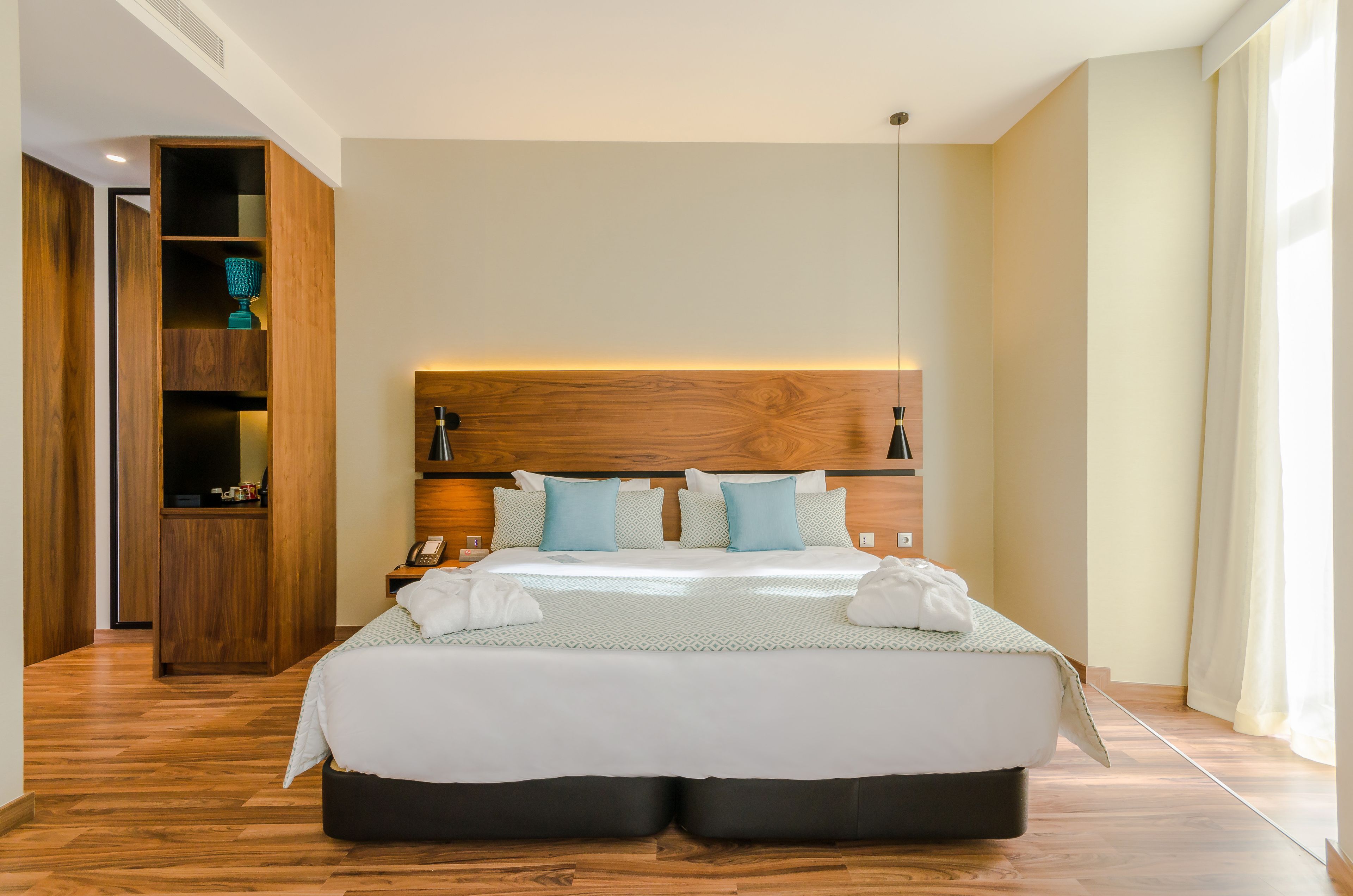 Una habitación de hotel moderna con una cama grande, cabecera de madera y estanterías empotradas.