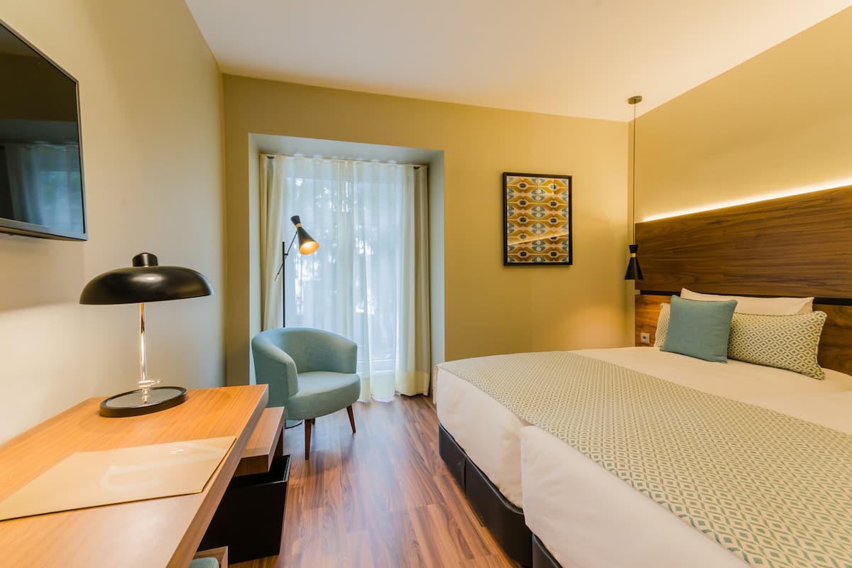 A hotel room with a bed, a desk, a chair, and a window with curtains.