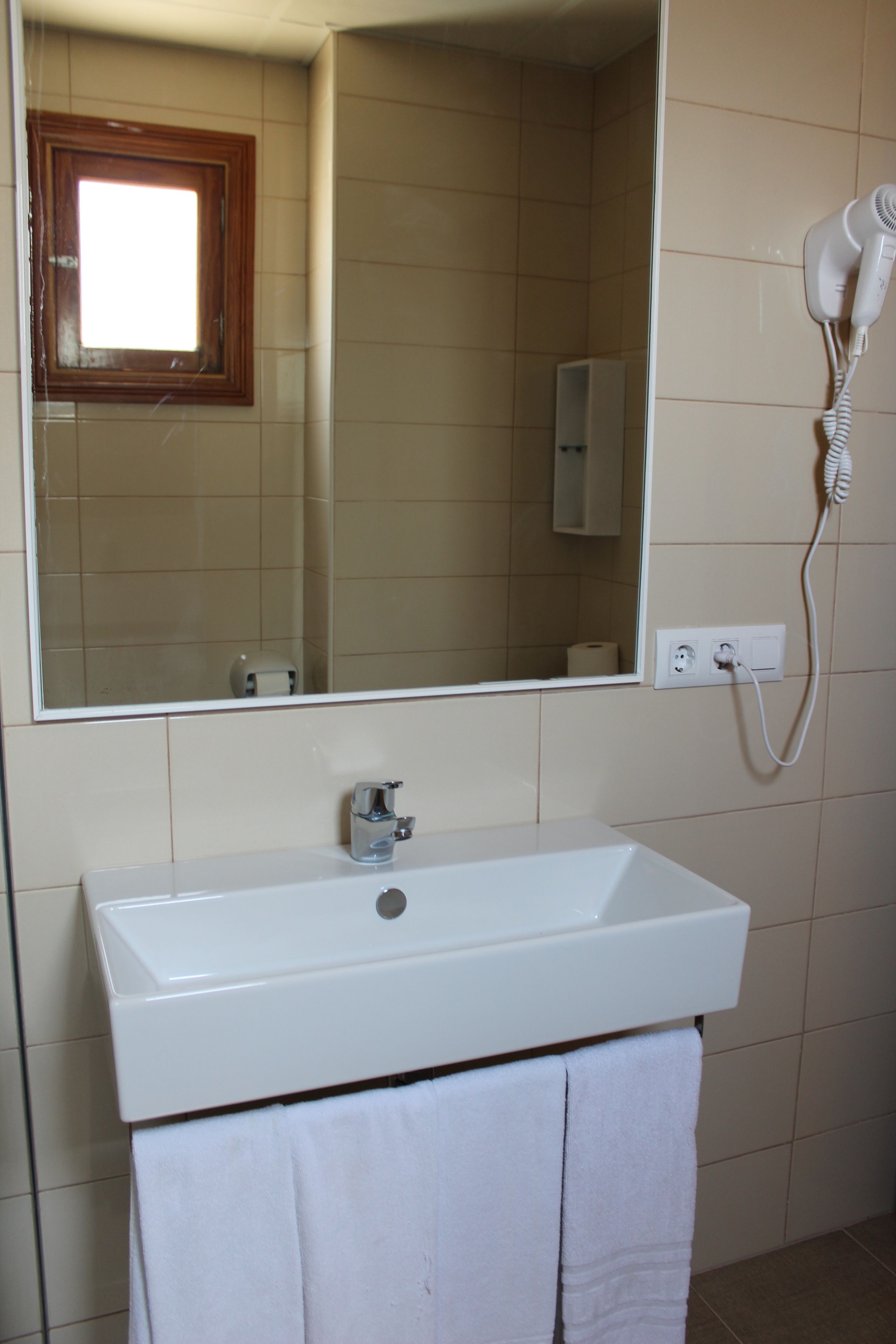 A bathroom with a white sink, a mirror, a hairdryer, and a towel rack.