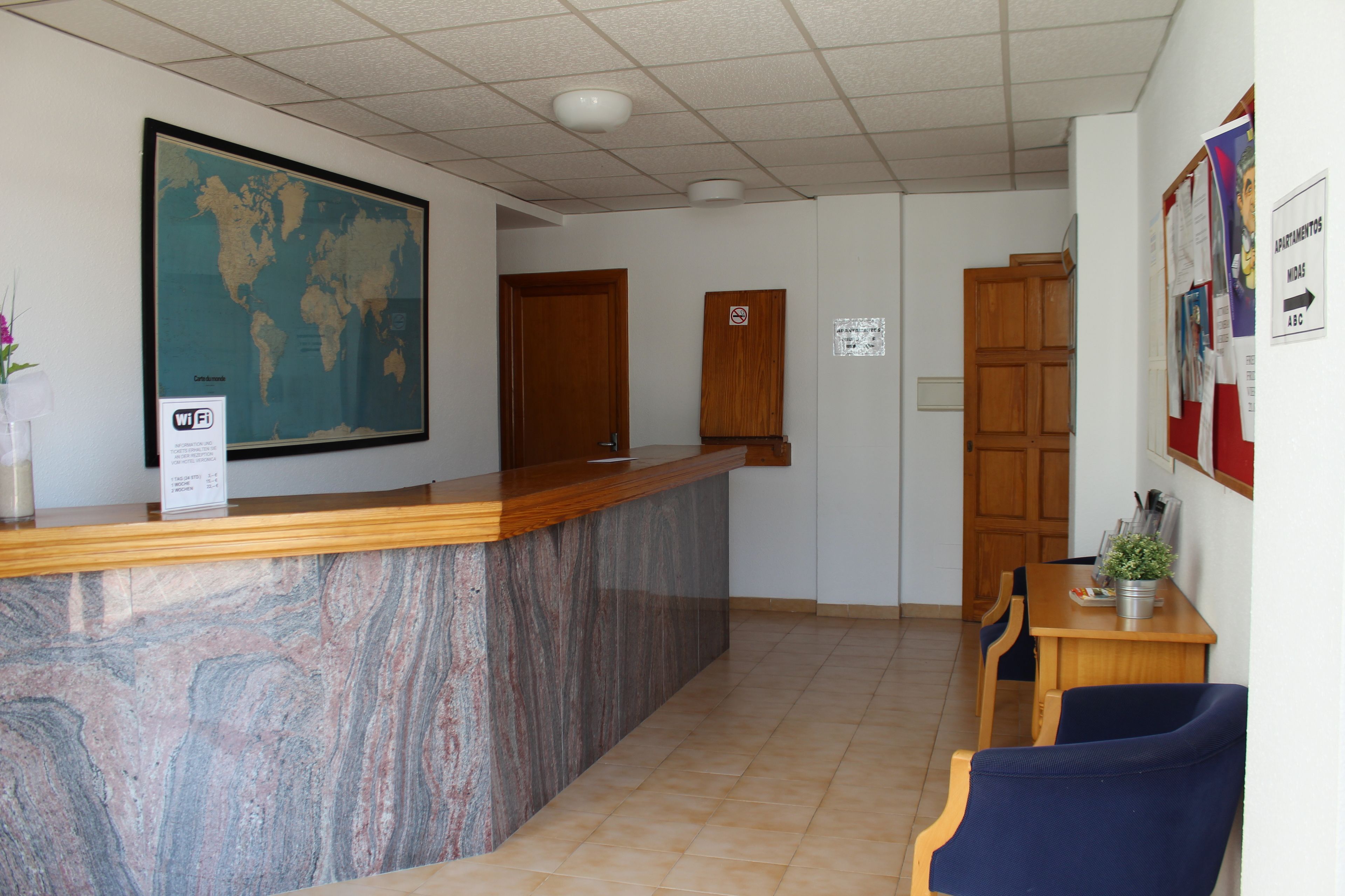 Una zona de recepción con mostrador de mármol, puertas de madera, un mapa mundial y un tablón de anuncios.