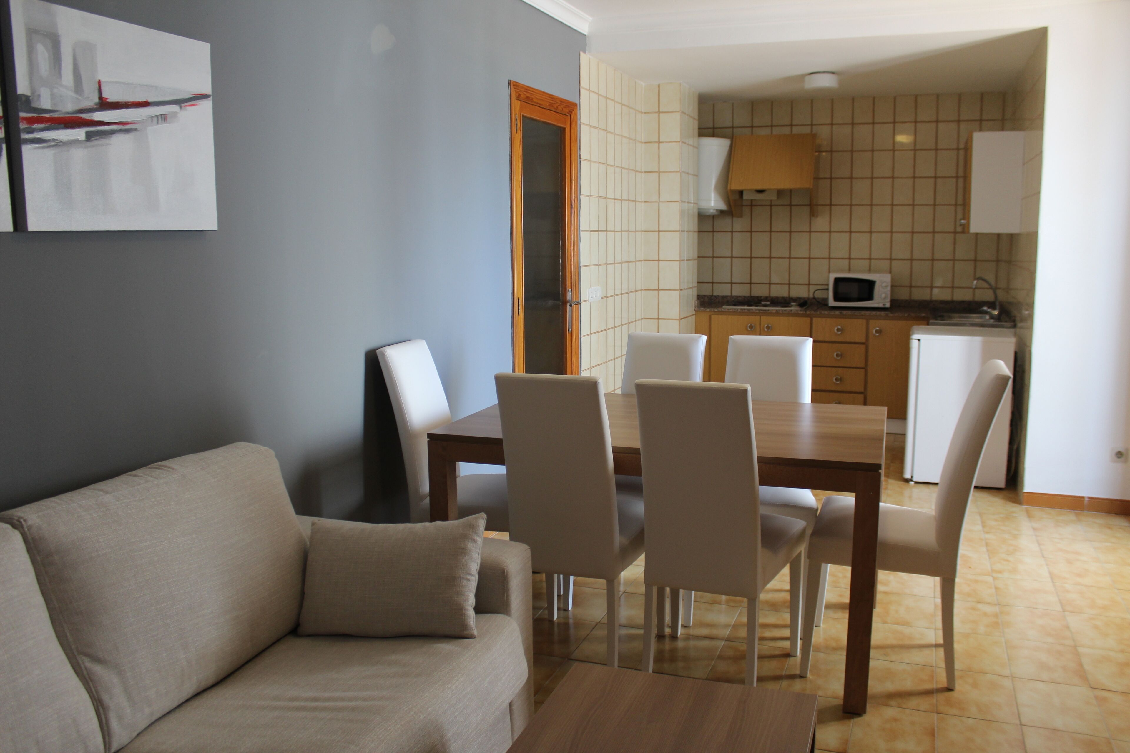 Un soggiorno con divano, tavolo da pranzo e sedie. Si intravede in secondo piano una cucina con forno a microonde e pensili.