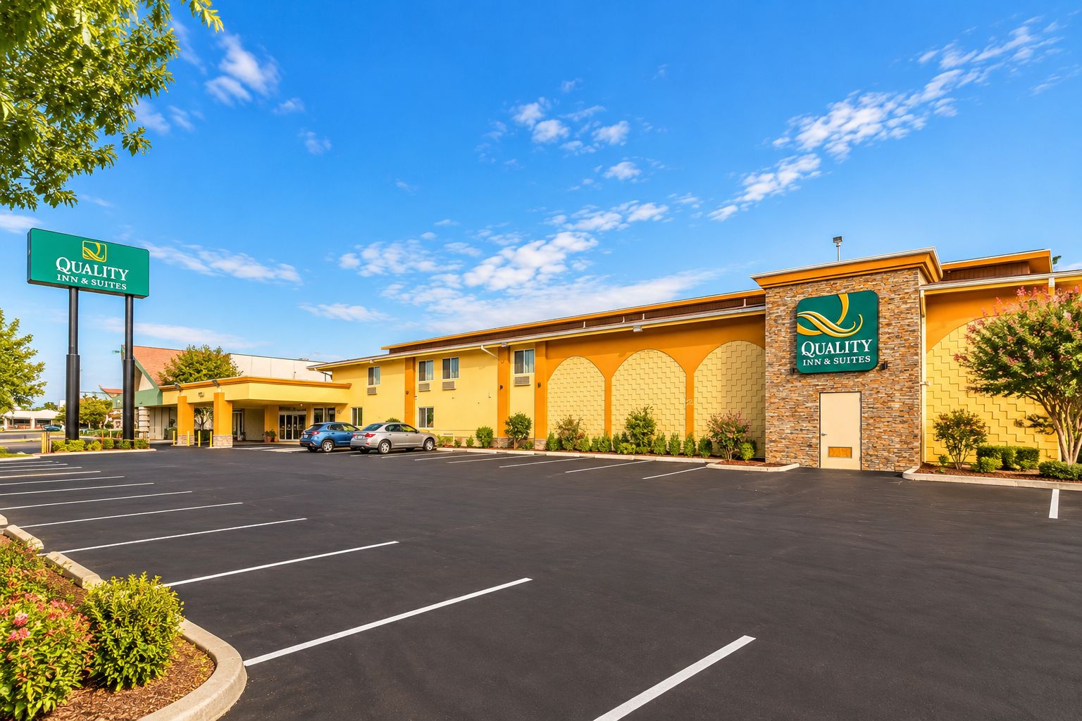 A Quality Inn & Suites with a parking lot, a clear sky, and a building with a yellow facade and green signage.