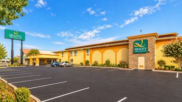 A Quality Inn & Suites with a parking lot, a clear sky, and a building with a yellow facade and green signage.